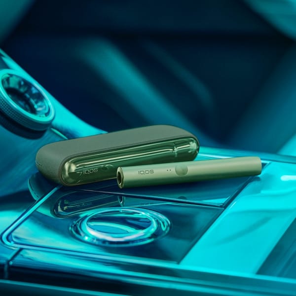 IQOS ILUMA ierīce Moss Green krāsā novietota automašīnā.