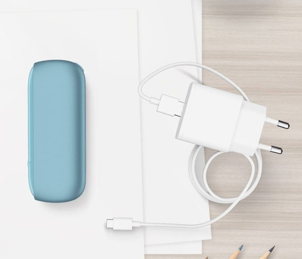 IQOS Originals DUO лежит на столе, рядом с ним находится кабель.