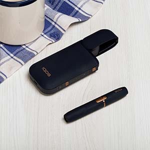 IQOS 2.4 черного цвета лежит на деревянном столе.