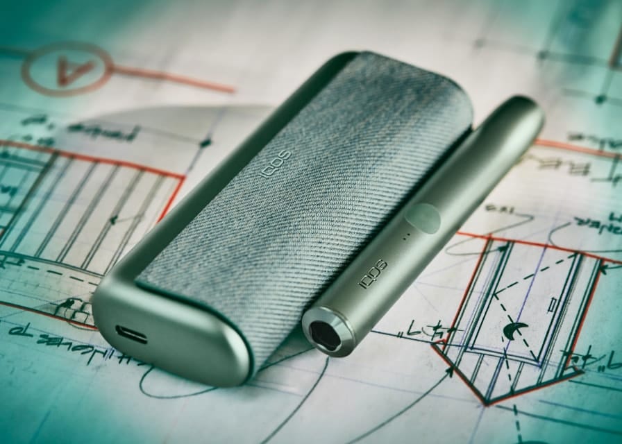Устройство IQOS ILUMA Prime цвета Moss Green на фоне с научной тематикой