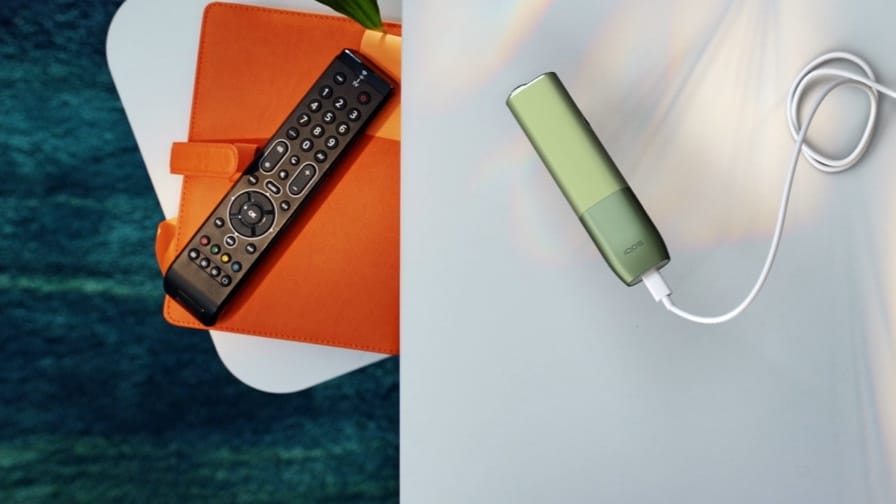 Ar rokām tiek strāvas adapterim pievienota IQOS ILUMA ONE ierīce.