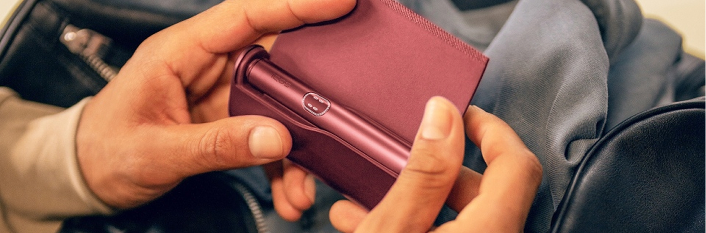 Руки держат IQOS ILUMA i PRIME над сумкой.