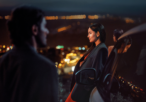 Женщина стоит ночью рядом с машиной.