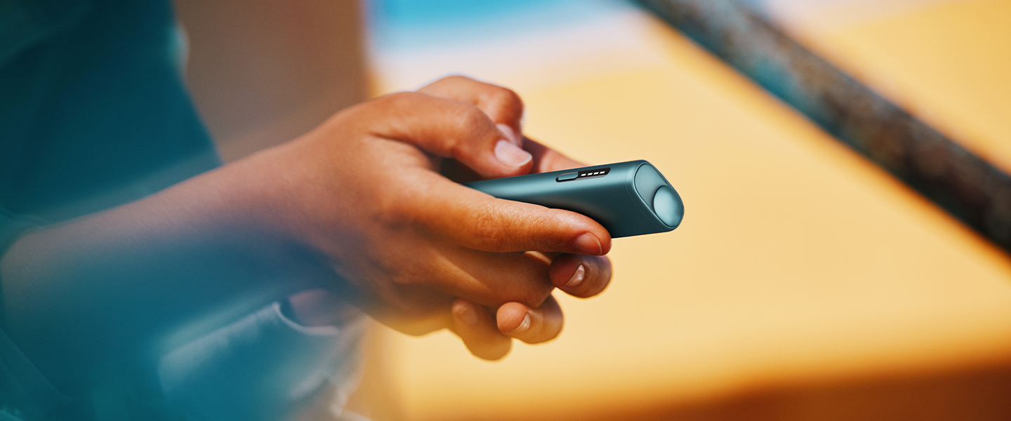 IQOS ILUMA Prime ierīce Moss Green krāsā uz zinātniskas tematikas fona