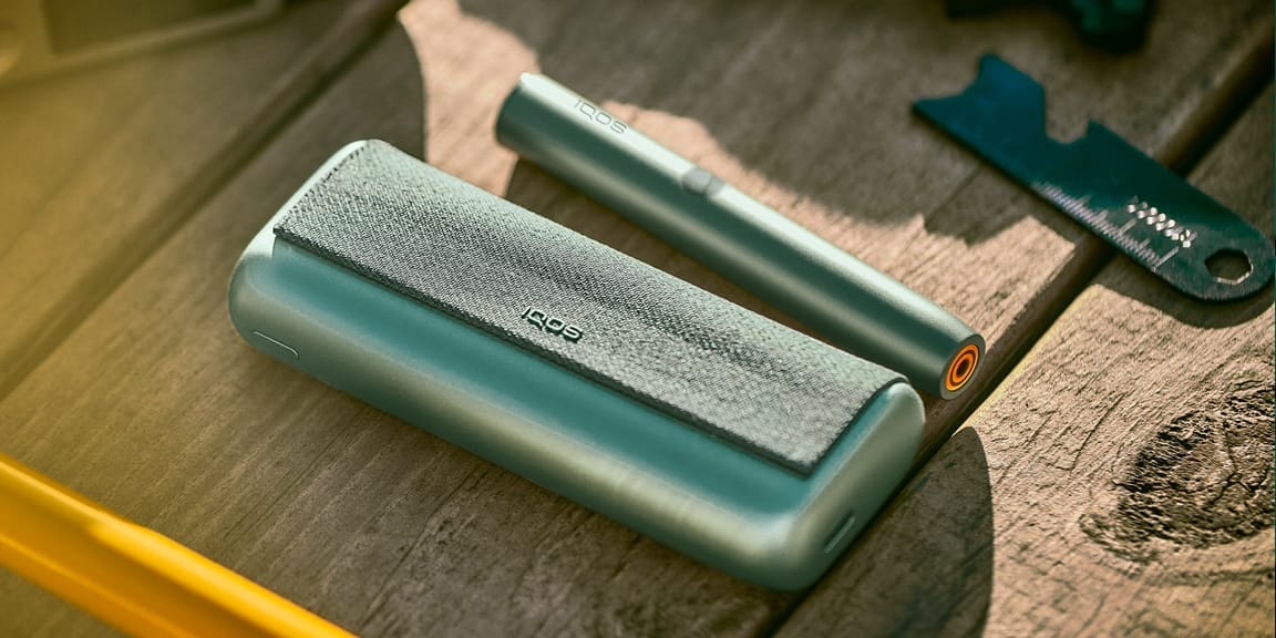 Устройство IQOS ILUMA PRIME Green Moss цвета, лежащее на деревянной поверхности.